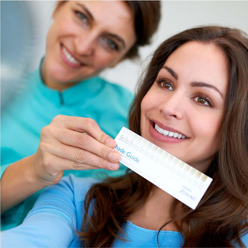Professionnel des soins dentaires qui tient un guide de tons devant un patient qui sourit
